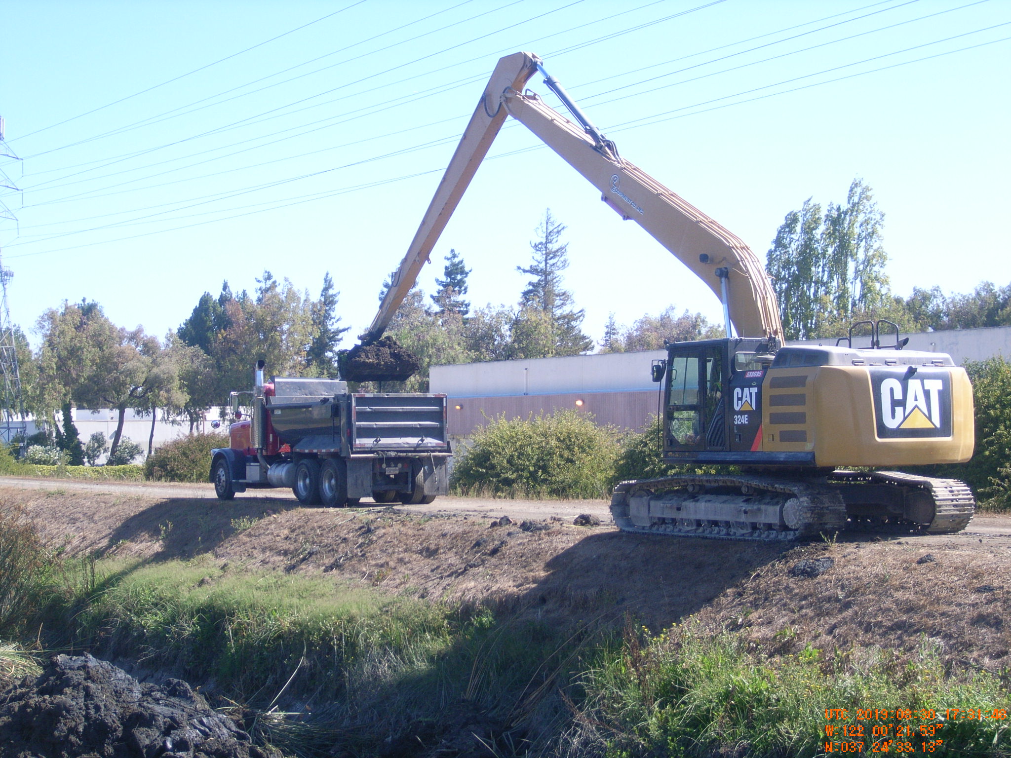 A house sits on a hillside with significant erosion, exposing soil and a damaged fence. Green grass peeks through the dirt.