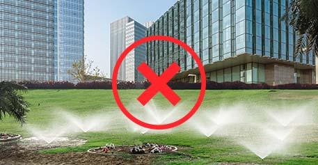 Commercial lawn with irrigation on and red x over it.