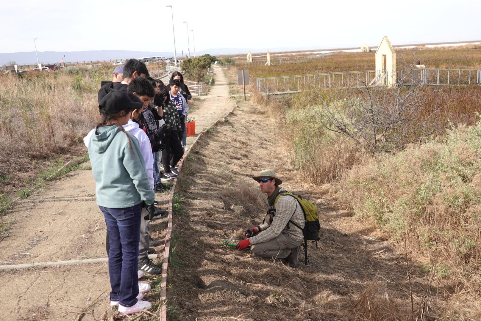 A group stand in front of an instructor outdoors to learn about water and bird habitat