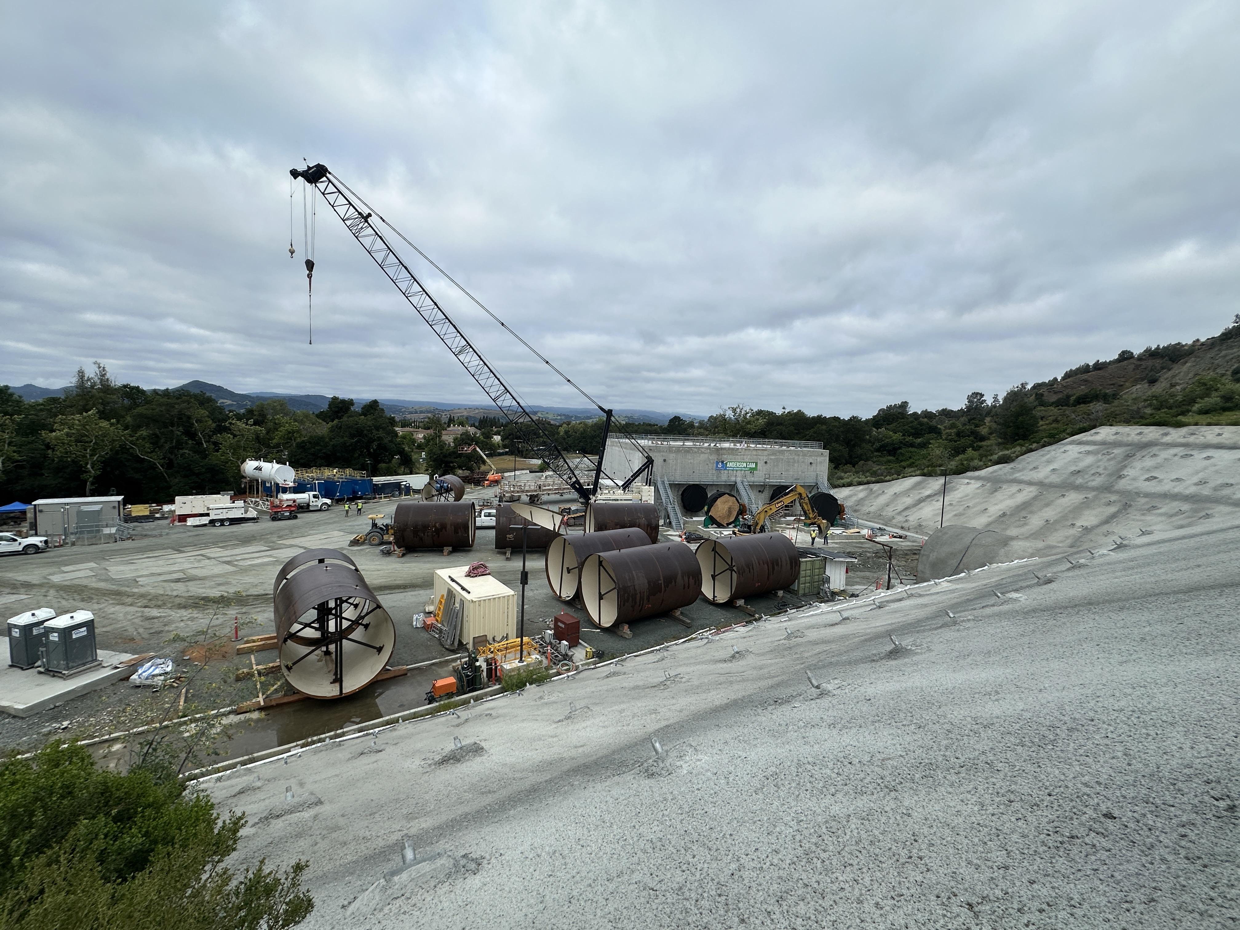 A view of the tunnel entrance on the right, and the diversion outlet structure. The staged, 13-foot diameter pipe will be placed inside the tunnel and will connect to the diversion outlet structure. April 2026.