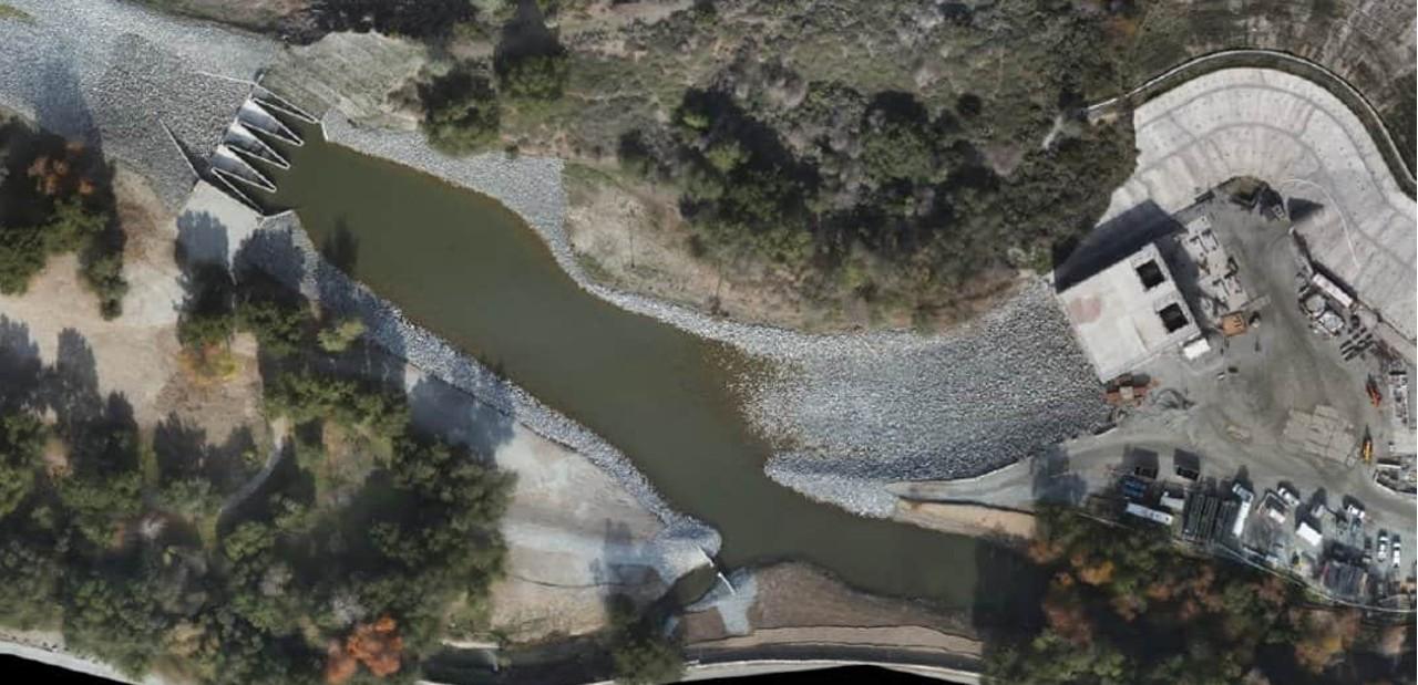 An aerial view of the North Channel weir (left), the South Channel weir (bottom), the diversion outlet structure, and the concrete retaining wall securing the hillside around the tunnel entrance.