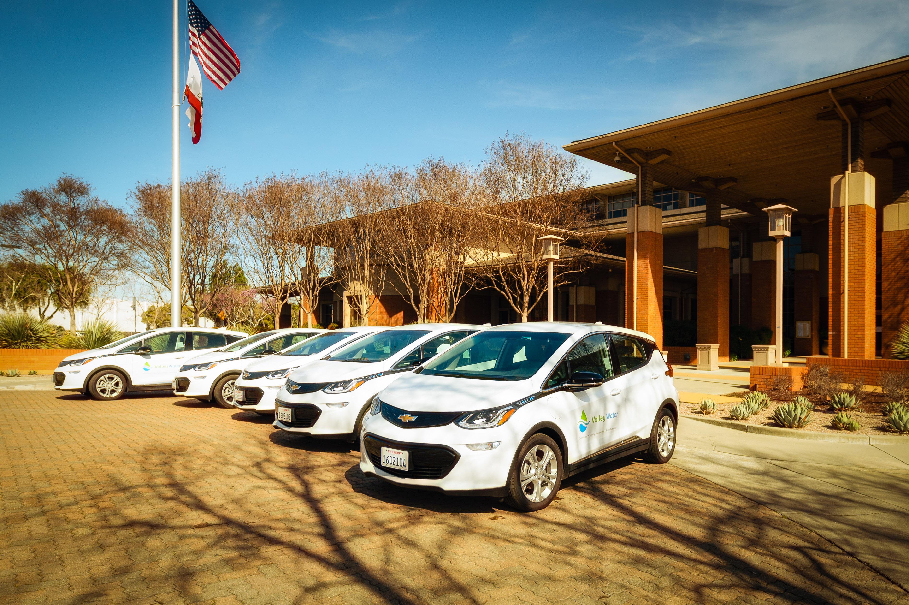 Five white EVs with the Valley Water logo sit outside a brown building