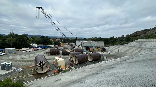 A view of the tunnel entrance on the right, and the diversion outlet structure. The staged, 13-foot diameter pipe will be placed inside the tunnel and will connect to the diversion outlet structure. April 2026